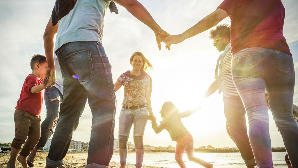 group of people, of all ages, holding hands in a circle with the sun beaming through the center
